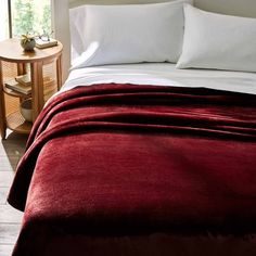 a bed with white pillows and red blankets on it, next to a small table