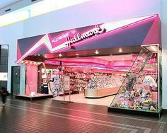 the inside of a store with people walking in front of it and there is a pink neon sign