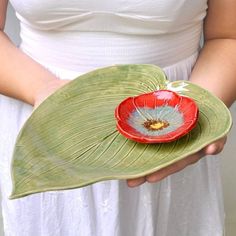 a woman holding a green leaf with a red flower in it