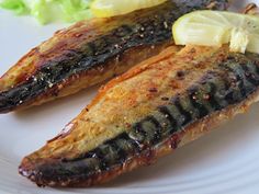 two grilled fish on a white plate with lettuce and lemon wedges