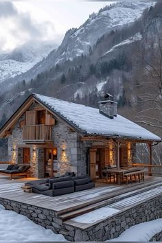 a stone house in the mountains with snow on the ground and lights on it's windows