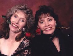 two women are posing for a photo with roses in their mouths and one is wearing a black dress