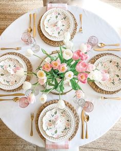 a white table topped with lots of pink and white flowers next to gold place settings