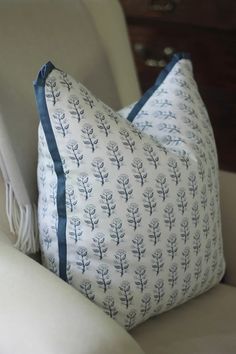 two pillows sitting on top of a white chair next to a pillow with blue trim