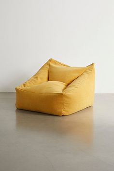 a large yellow bean bag chair sitting on top of a cement floor next to a white wall