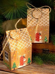 two small gift bags sitting on top of a wooden table next to a pine tree