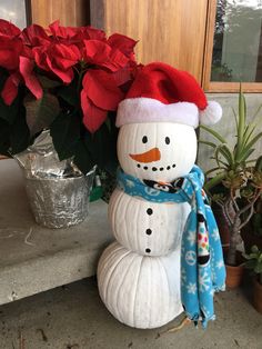 a snowman sitting next to a potted plant with poinsettis in the background