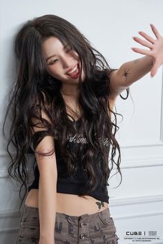 a woman with long hair and tattoos posing for a photo in front of a white wall