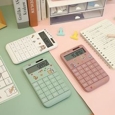 three calculators sitting on top of a table next to books and paper clips