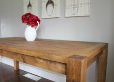 a vase with red flowers sitting on top of a wooden table next to two pictures