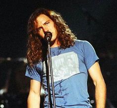 a man with long hair standing in front of a microphone and wearing a blue shirt