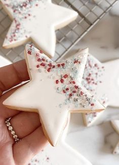 a hand holding a star shaped cookie with sprinkles on it next to other cookies