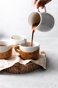 someone pouring coffee into two cups on top of a wooden tray