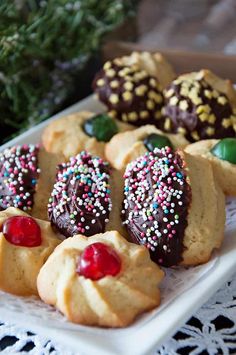 several cookies with sprinkles and chocolate on a white platter next to green leaves