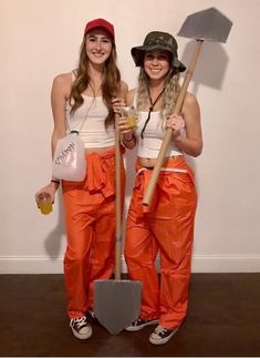 two women in orange pants and hats holding shovels