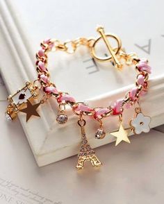 a gold bracelet with charms and flowers on it, sitting next to a white box