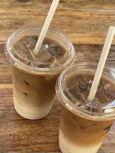 two iced coffees sitting on top of a wooden table with straws in them