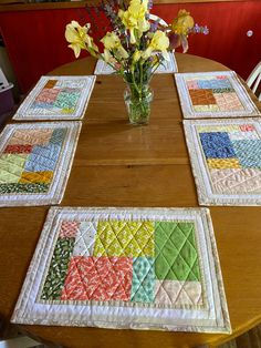 a vase with flowers sitting on top of a table next to four quilted placemats