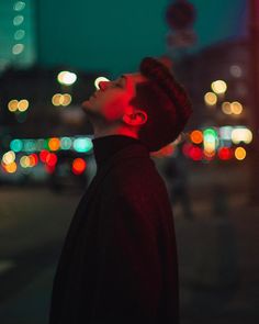 a man standing on the street with his head turned to the side and lights in the background