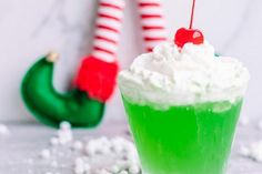 a green drink with whipped cream and a candy cane in the background on a table