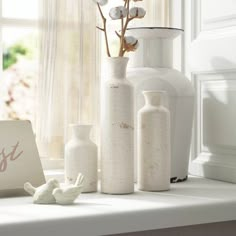 white vases with flowers in them sitting on a window sill next to a sign