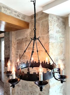 a chandelier with lit candles hanging from it's sides in front of a stone wall