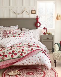 a bed covered in red and white quilts next to a window with christmas decorations on it