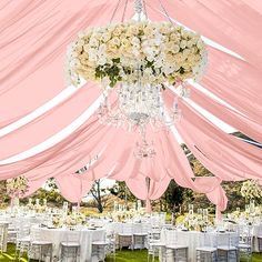 a chandelier hanging from the ceiling over tables covered in pink and white linens