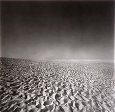 black and white photograph of sand dunes with dark sky in the background at low tide