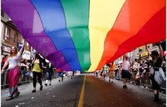 a large rainbow flag is being carried down the street by people on roller skates