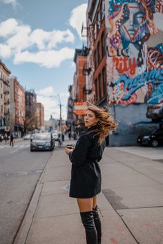 a woman is standing on the sidewalk looking at her cell phone while she's wearing thigh high boots