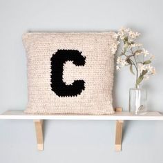 a crocheted pillow sitting on top of a shelf next to a vase with flowers