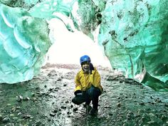 a man in yellow jacket and blue helmet walking through an ice cave