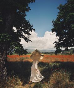 a woman in a white dress and straw hat walking through a field with poppies