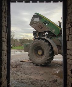 a tractor is parked in the mud near a brick wall and door way that leads to a parking lot