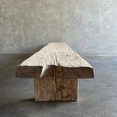 a wooden bench sitting on top of a cement floor next to a wall with white walls