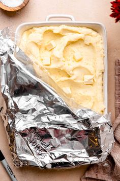 a pan filled with mashed potatoes on top of tin foil next to a spoon