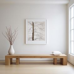 a white vase sitting on top of a wooden table next to a painting above it