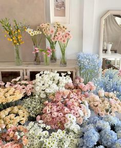 a bunch of flowers that are in vases on a table with mirrors behind them