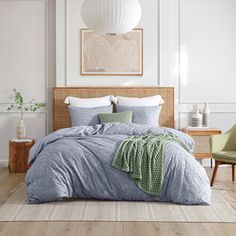 a bedroom with white walls and wood flooring has a large bed covered in blue linens