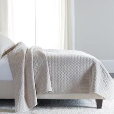 a bed with a white comforter on top of it next to a window in a room