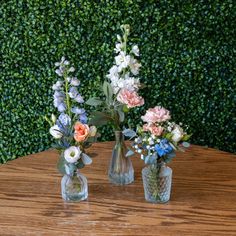 three vases with flowers are sitting on a table in front of a green wall