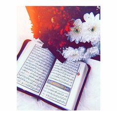 an open book sitting on top of a table next to white flowers and a vase