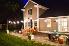 an outdoor patio with chairs and lights on the side of it at night, lit up by string lights