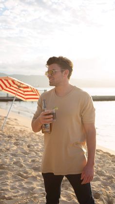 a man standing on the beach holding a drink