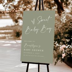 an easel with a baby shower sign on it sitting in front of some flowers