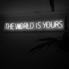 a neon sign that says the world is yours on it's wall above a potted plant