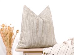 a white pillow sitting on top of a wooden table next to a vase with dried flowers