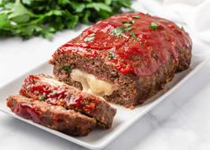 sliced meatloaf with sauce and cheese on a white plate next to parsley