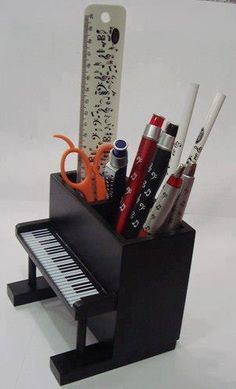 a small black piano with pens, scissors and pencils in it's holder